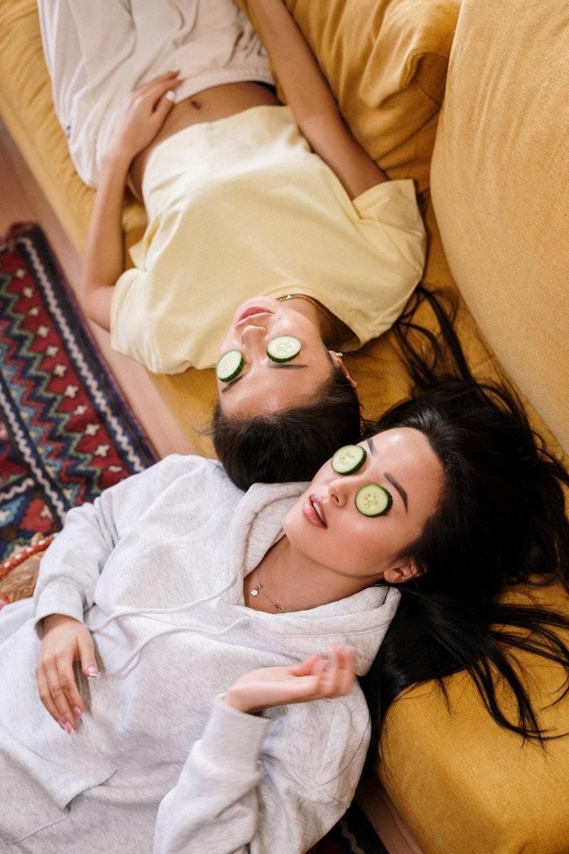 Two woman with cucumbers over eyes doing their skincare routine.