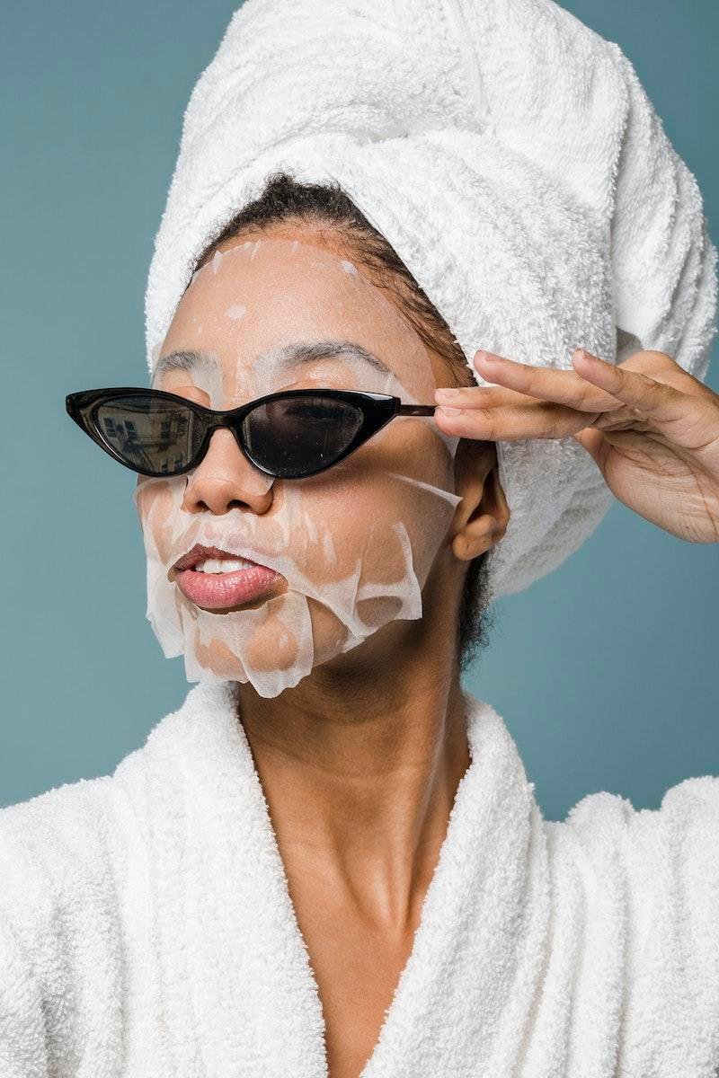 Woman with glass skin wearing a sheet mask and hair towel